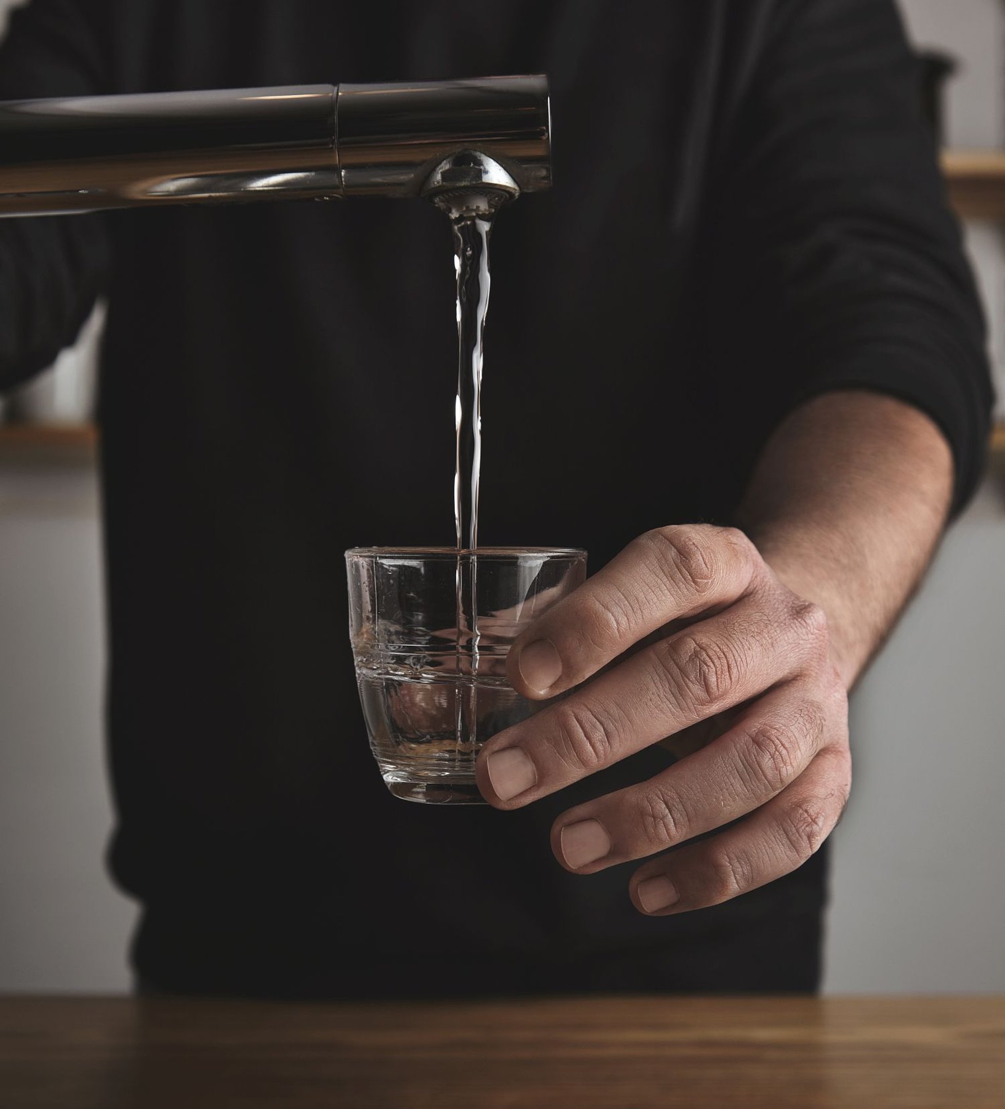 Eine Person füllt ein Glas mit Wasser aus einem modernen Wasserhahn über einem Waschbecken.